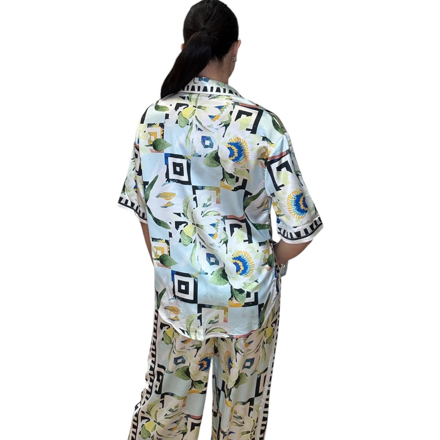 Back view of a woman wearing a satin sky button-down shirt and pants set with a colorful print.