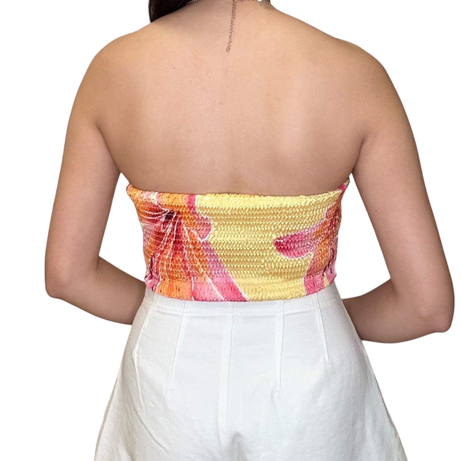 Back view of a strapless satin scarf top with a pink floral design paired with white shorts.